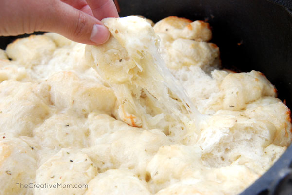 pulling a piece of cheesy garlic bread bites out of dutch oven